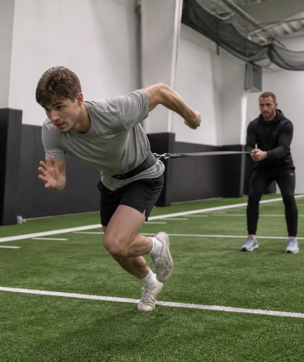 Athlete performing a resisted sprint start on indoor turf with coach assisting